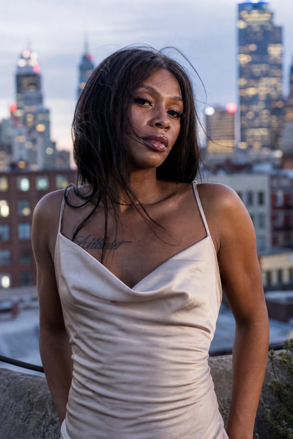 Black transgender woman in a satin dress on a city rooftop at dusk