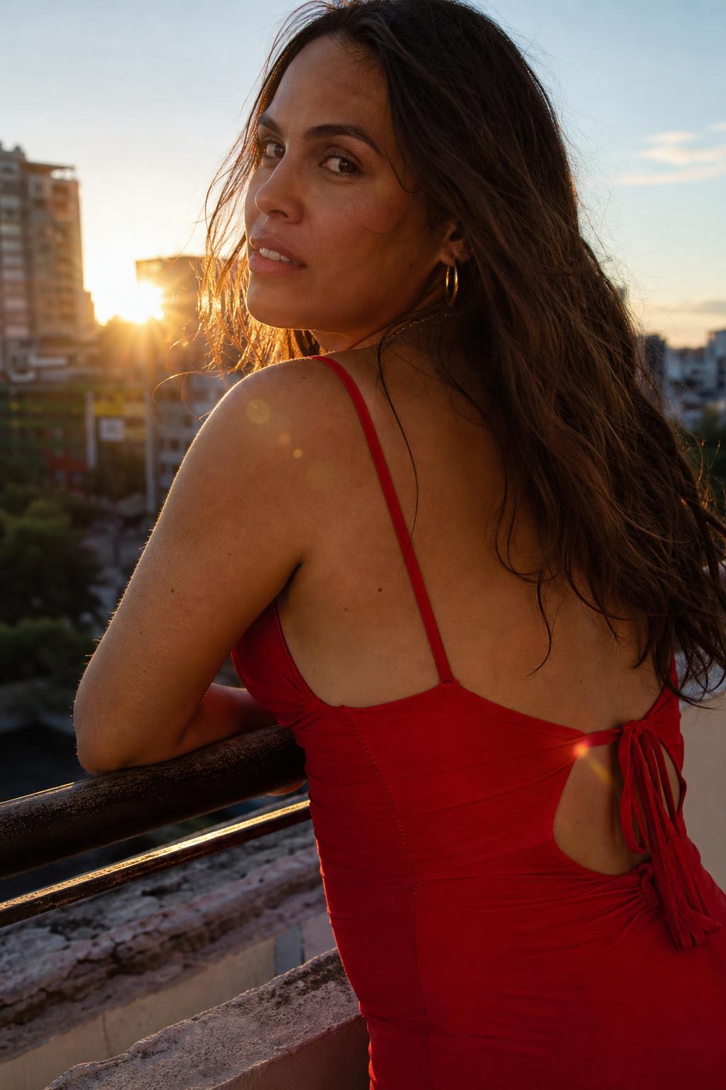 Latina transgender woman in a red dress on a balcony at golden hour