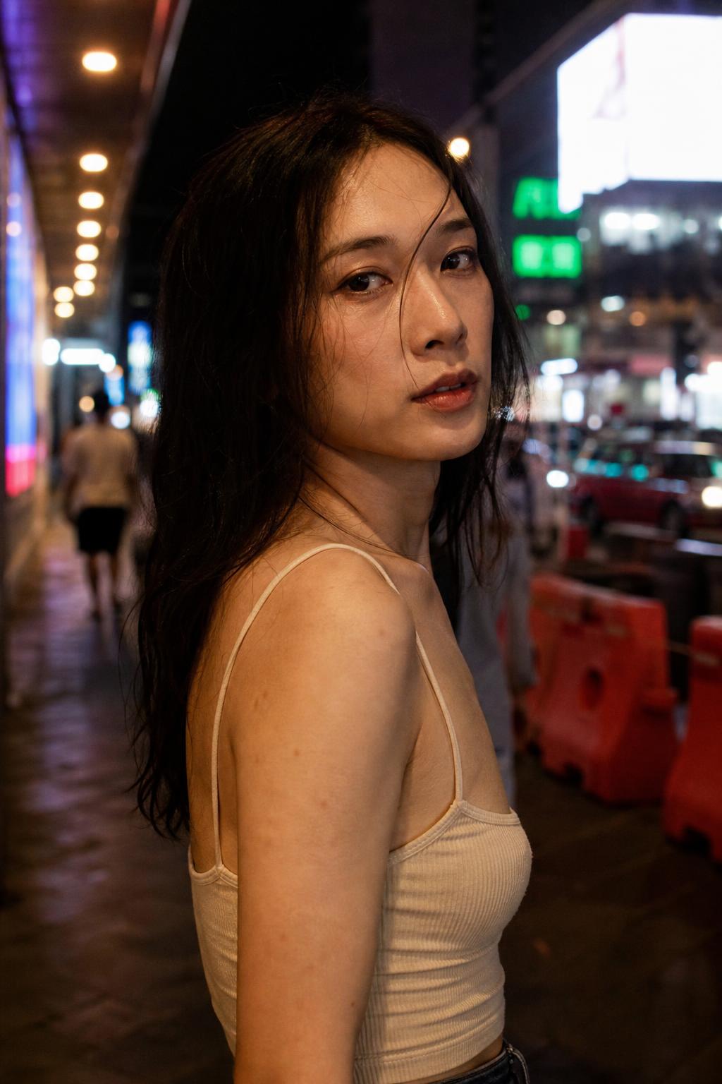 East Asian transgender woman on a neon lit city street at night
